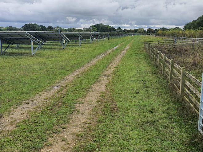 Solar panels at a solar farm seen from the back next to agricultural land