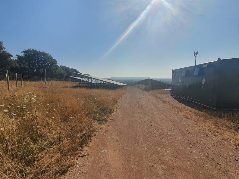 Solar panels and infrastructure on a plot of agricultural land either side of an access track